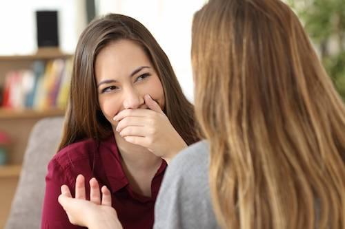 woman facing another woman covering her smile with her hand