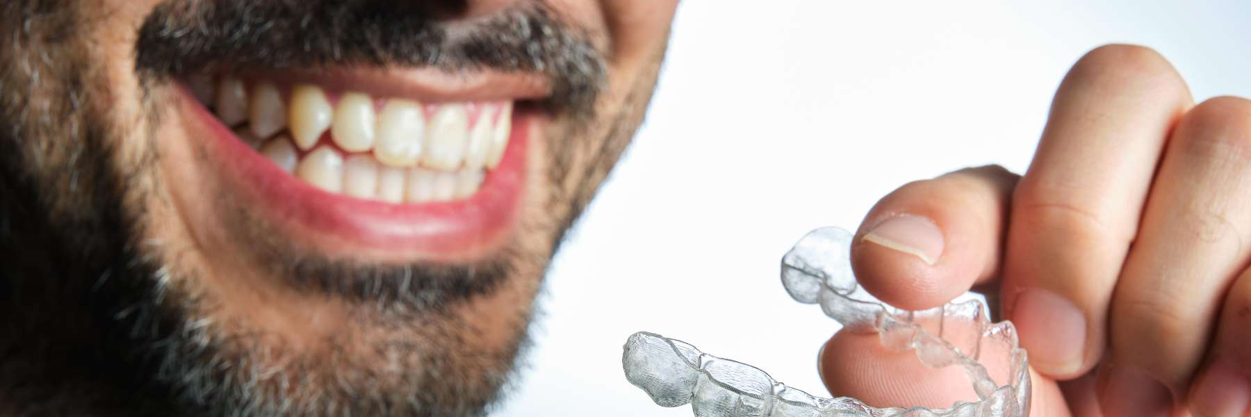 Man with straight full set of teeth holds his clear aligner in Tampa