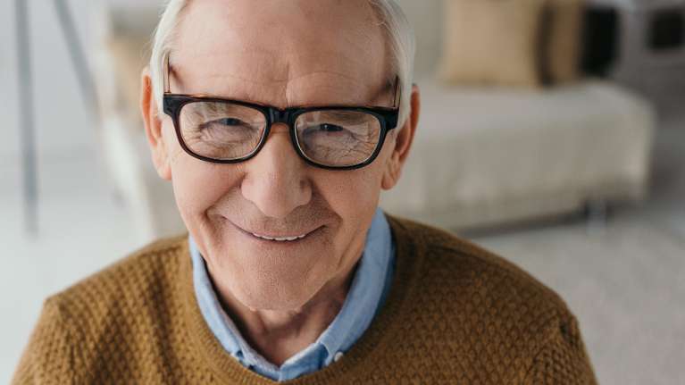 Old man wearing eyeglasses smiling with his implant denture in North Tampa