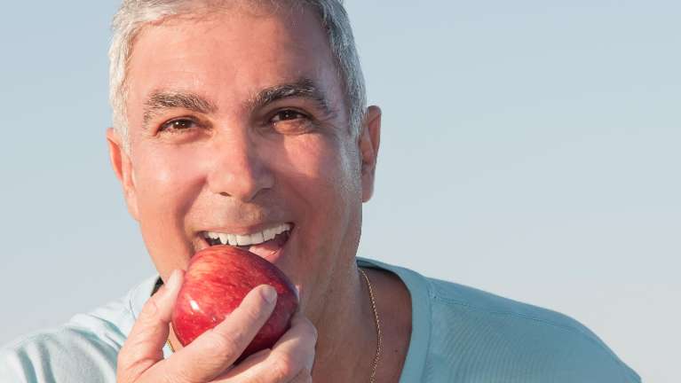 man with dental crowns holding an apple