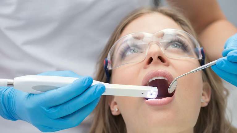 A young woman sits in a dental chair, her mouth open wide for a dental cleaning procedure